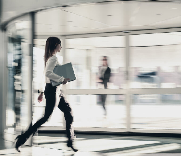 Blurred Businesswoman Walking Through Office Entrance Using Smart Phone